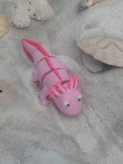 Pink axolotl toy on sandy surface with shells and sandcastles in the background